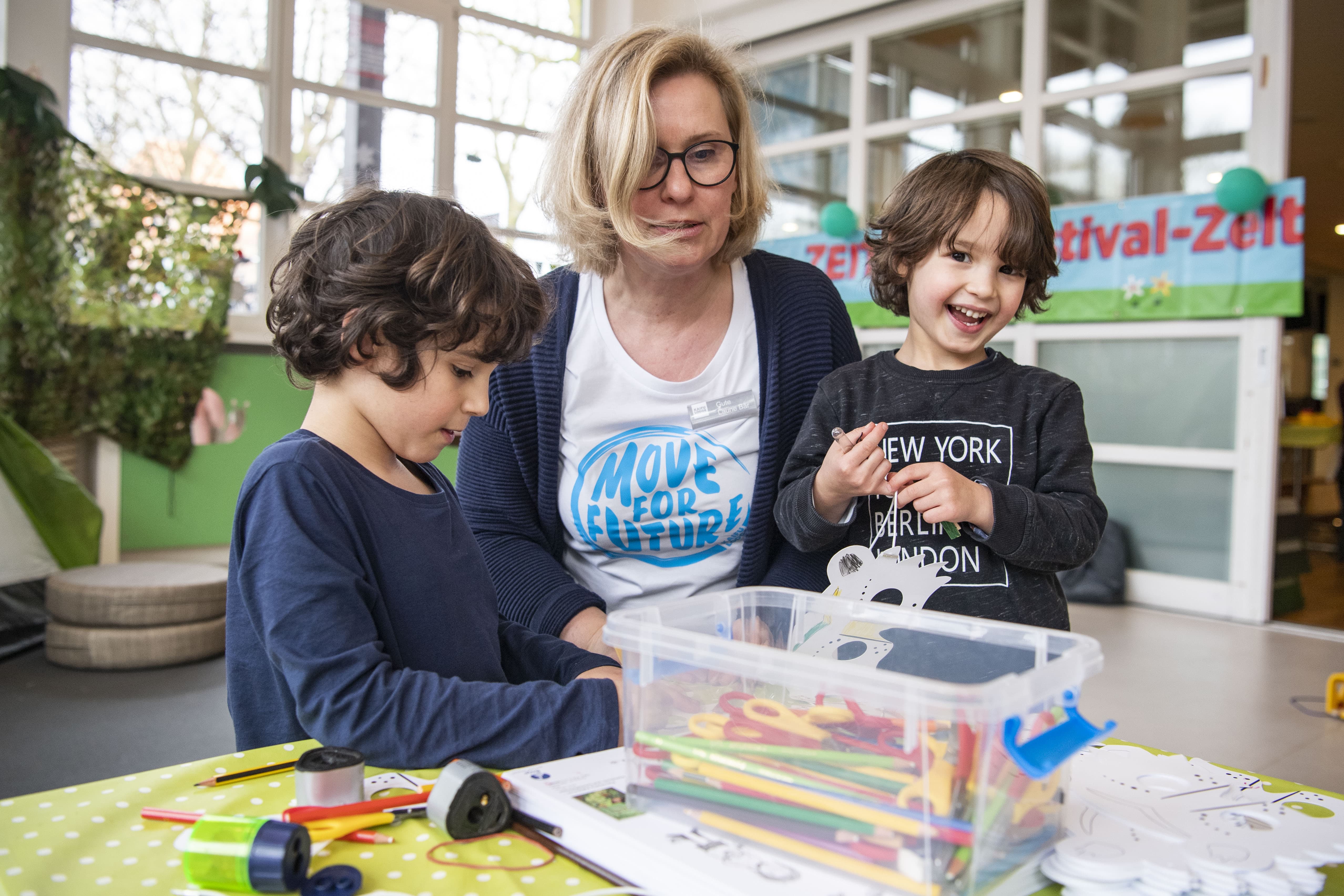 Eine Mitarbeiterin aus der Kinderbetreuung malt und bastelt mit zwei Kindern