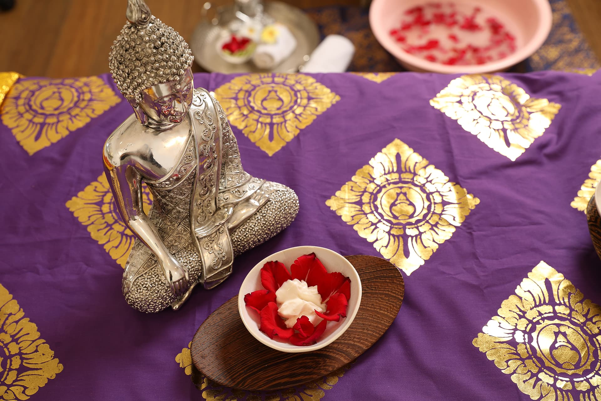 A bowl with rose petals and a Buddha figure on a colorful cloth in the massage room of a gym