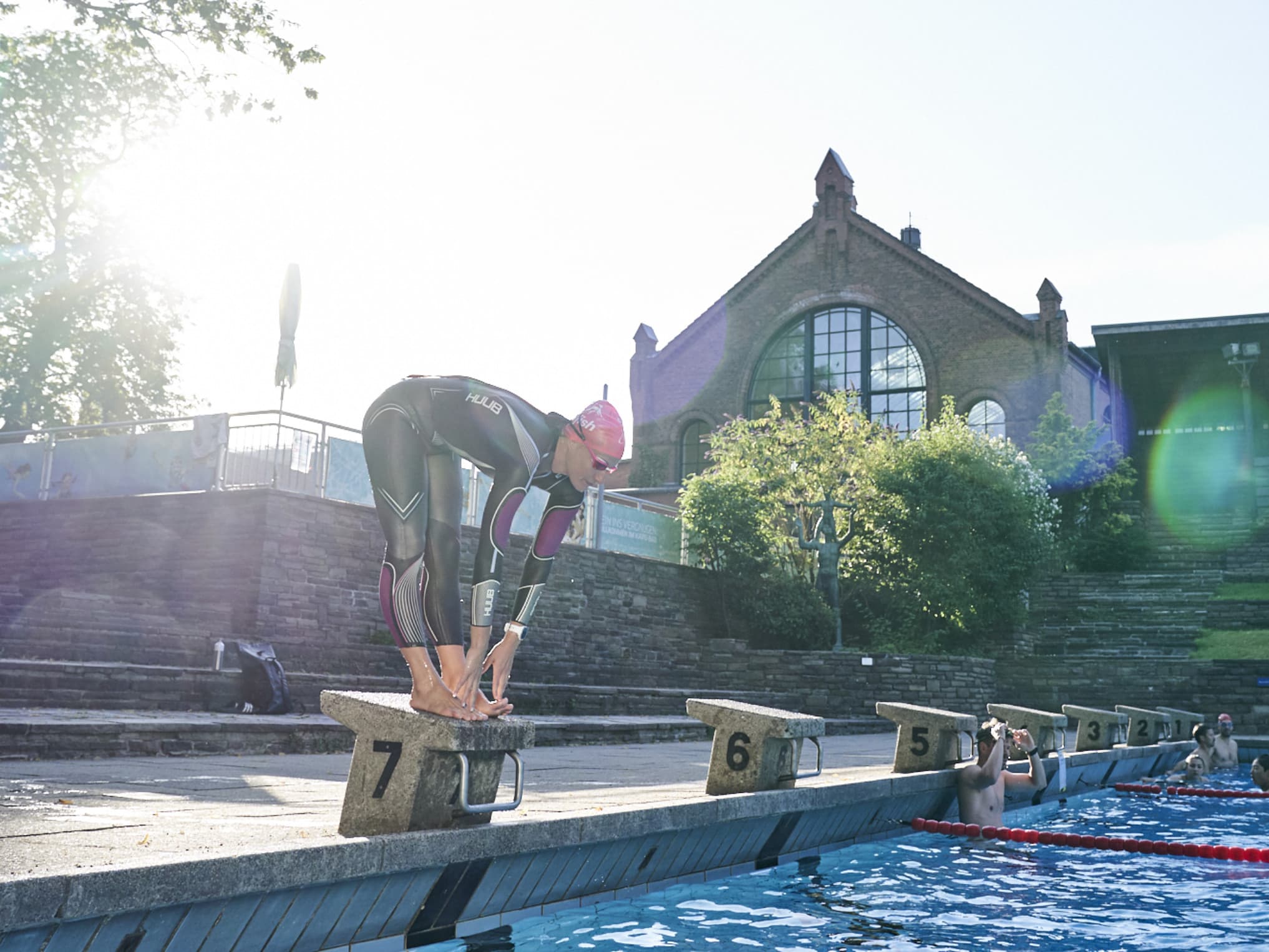 Schwimmer steht am Beckenrand eines Schwimmbads bereit zum Absprung ins Becken eines Freibads