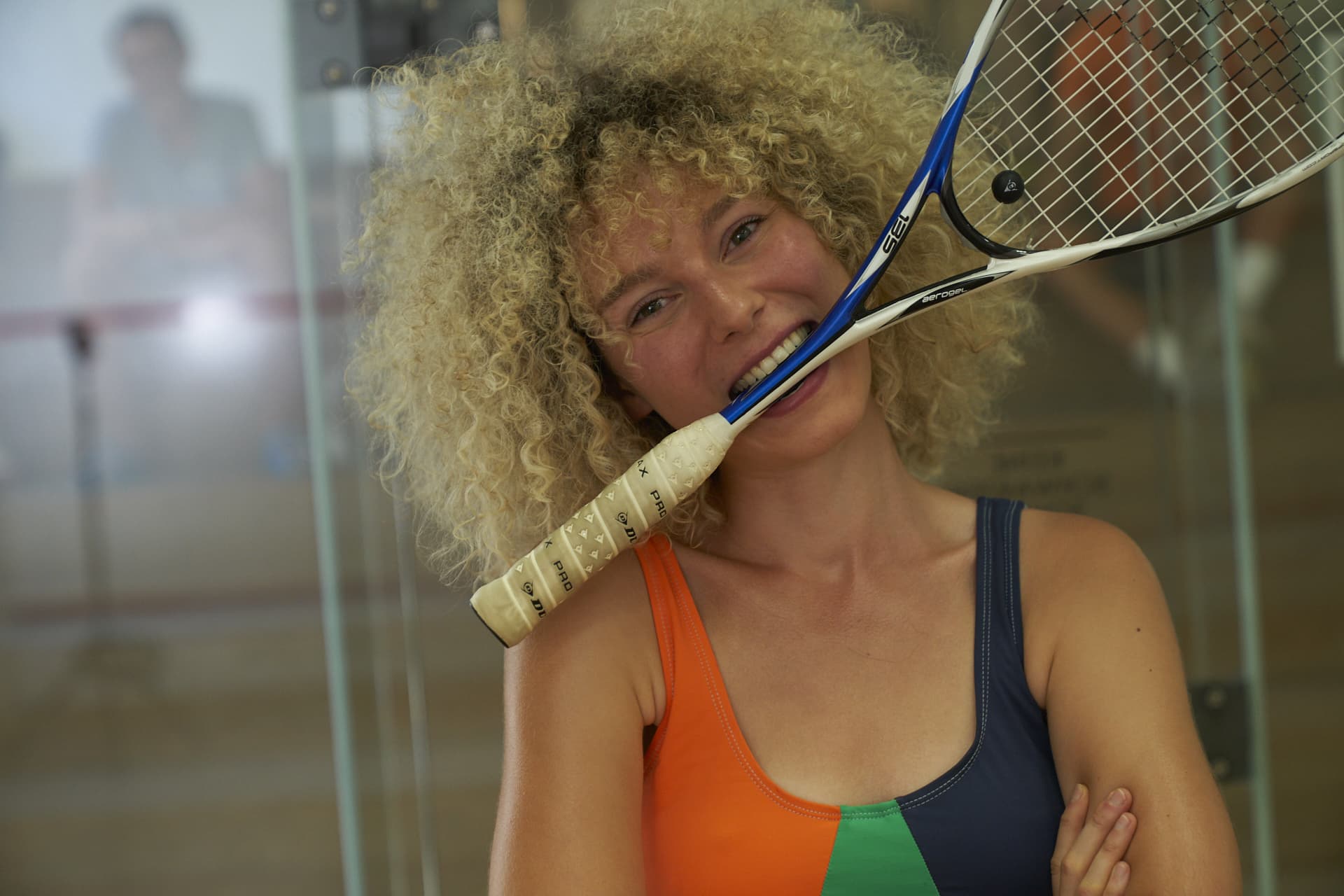 Eine gut gelaunte Squash-Spielerin mit ihrem Schläger im Mund auf dem Squash Court