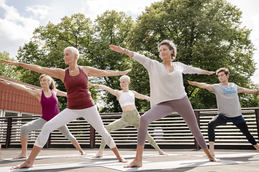 Yogateilnehmer*innen in der Kriegerposition beim Yoga auf der Terrasse