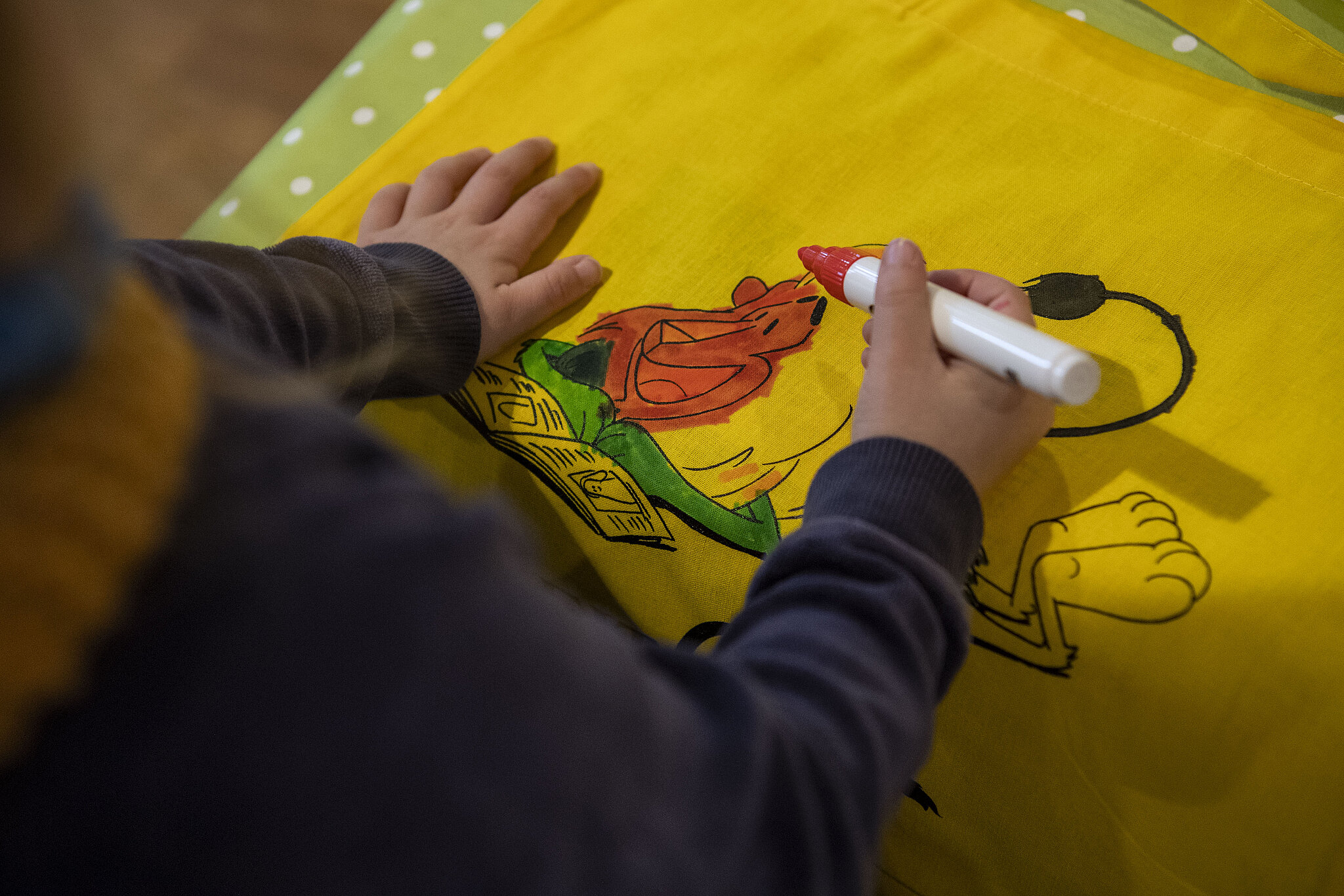 Ein Kind bemalt ein Stück Stoff in der Kinderbetreuung